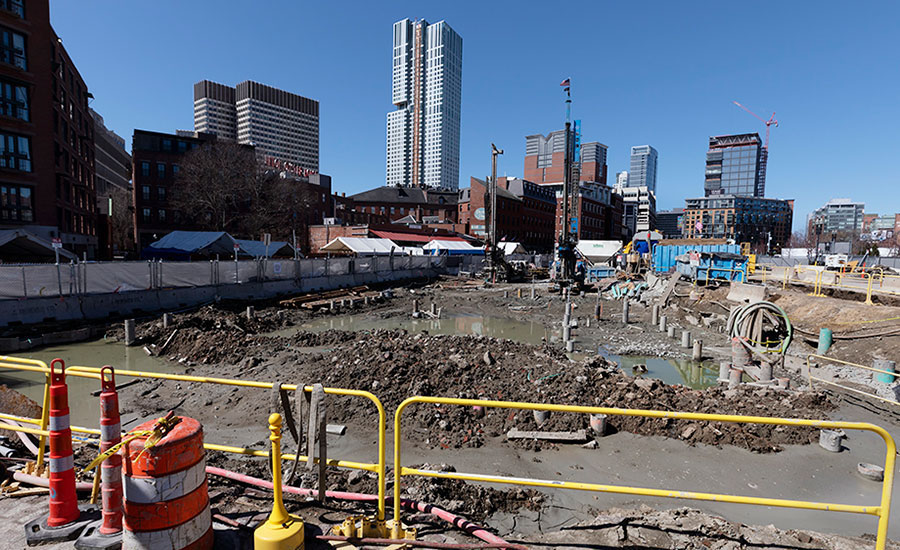 Construction worker operating heavy equipment, possibly a backhoe or excavator, on a job site.